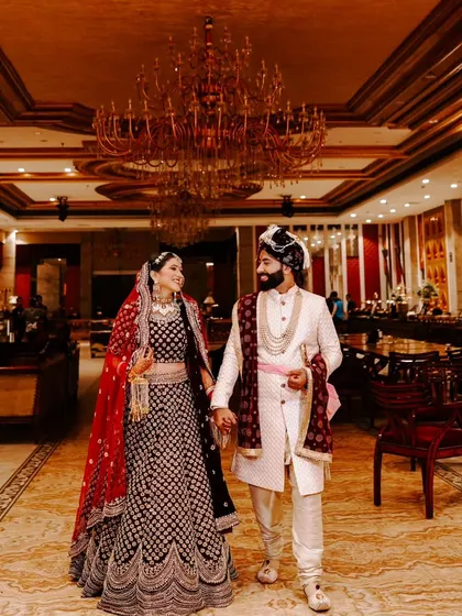 A beautiful, wide shot of a couple walking hand-in-hand through a grand, chandelier-lit hall on their wedding day.