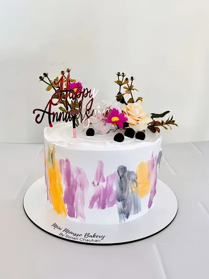 A colorful anniversary cake with a painted buttercream effect. The fresh flowers on top add a natural, rustic touch to the modern design.