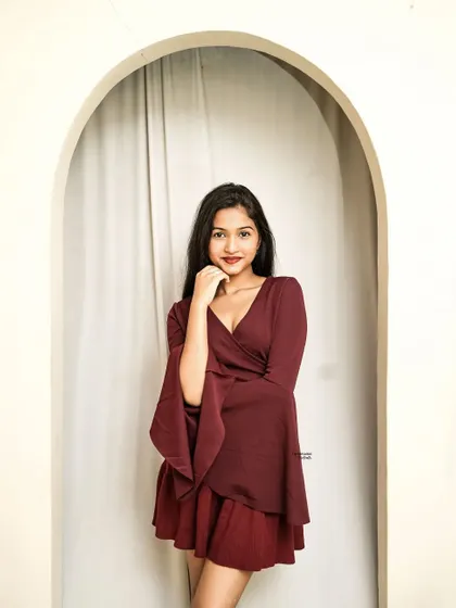 A welcoming pose in an arched doorway, the model's smile and the flowing sleeves of her maroon outfit create a beautiful frame.