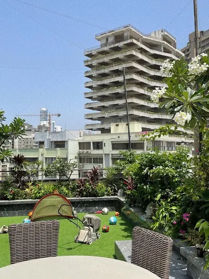 A family's terrace garden designed to be both beautiful and functional. We used durable artificial turf for a play area, surrounded by lush planters filled with flowering trees and shrubs, creating a safe and green space against the Mumbai skyline.