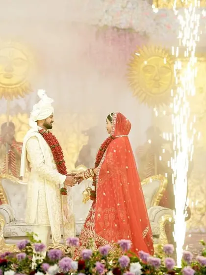 A romantic Jaimala moment, with the couple framed by golden pyrotechnic sparks. The soft lighting and traditional props create an intimate yet spectacular setting for their union.