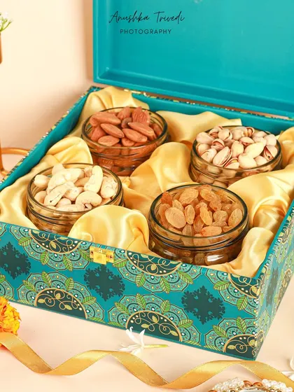 A luxurious dry fruit hamper for Diwali, with a rich teal and gold design, styled with fresh flowers and a ribbon.