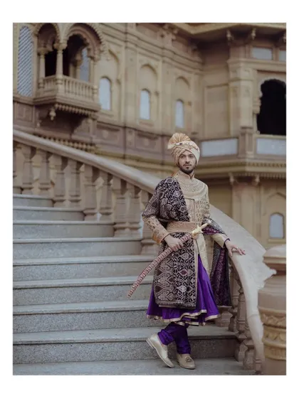 A full-length portrait of the groom in his royal attire, posing with a sword on the grand staircase of the palace venue.