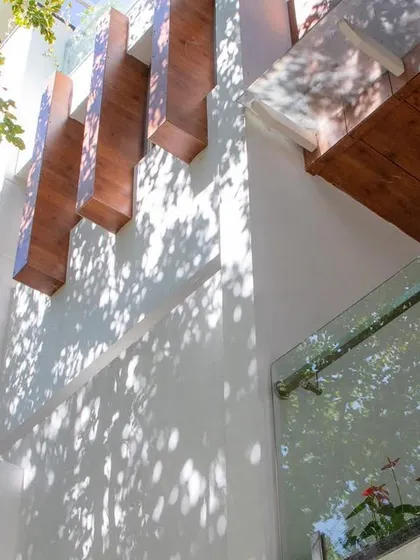 An upward shot of the 'Isha-Vaasyam' home, where protruding wooden elements create a rhythmic pattern against the white wall, playing with sunlight and shadow.