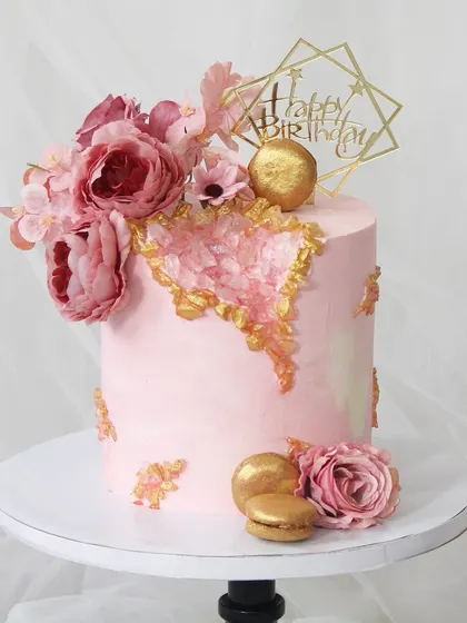 A stunning pink geode cake that combines modern trends with classic beauty. The cake features a crystallized sugar geode in the center and is decorated with beautiful pink sugar flowers and macarons.