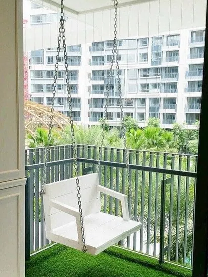 A simple, clean design for a small urban balcony. The main feature is a modern white swing, which provides a relaxing spot to enjoy the view. The artificial grass floor adds a touch of green and softness underfoot.