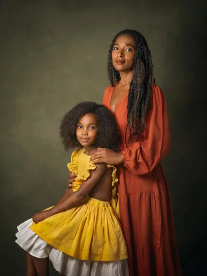 This portrait captures the beautiful resemblance and bond between mother and daughter. The coordinated colors of their outfits and the simple, classic posing result in a timeless image that feels both formal and full of warmth.