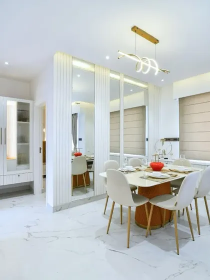 A bright and airy dining area featuring mirrored wall panels and fluted details. The neutral-toned furniture and a modern, sculptural light fixture create a warm and relaxed ambiance perfect for family meals.