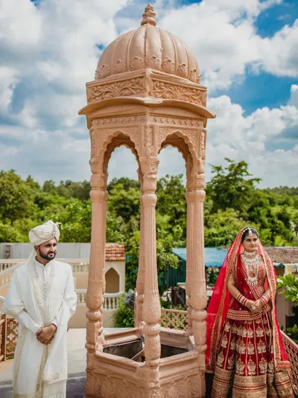 A formal portrait of the couple standing under a stone gazebo. This shot highlights their regal attire and the stunning architecture of their wedding venue.
