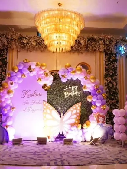 A full view of the grand stage setup for the butterfly-themed party. The combination of the large balloon arch, central backdrop, and stage lighting creates an impressive focal point in the banquet hall.