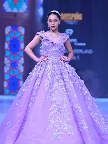 A vision in lavender. This regal ball gown features a cascade of 3D floral appliqués over a glittering tulle skirt, designed to make you feel like you are walking through a field of flowers.
