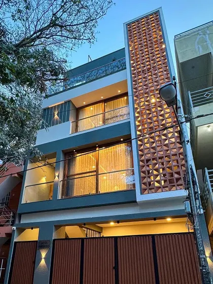 The same compact residence at dusk, where internal and external lighting accentuates the vertical brick jali and modern architectural form.