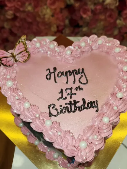 A sweet, heart-shaped cake for a 17th birthday. The pink frosting, pearl details, and delicate butterfly make it a lovely choice for a teenager.