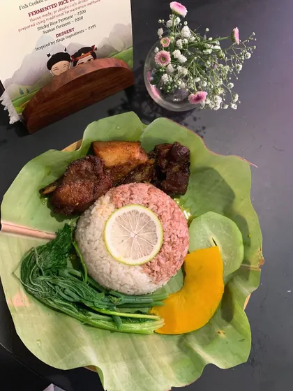A beautifully arranged Naga meal served on a lotus leaf. This plate features pork, red rice molded with a slice of lemon, boiled greens, and a slice of pumpkin, showcasing a simple yet elegant presentation.