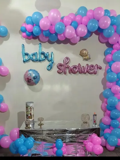 A simple baby shower setup at home. The decor includes a pink and blue balloon arch and foil letters spelling 'Baby Shower'.