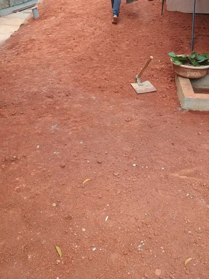 Our backyard preparation leaves a cleared red-soil surface beside the tiled path, with tools still on the ground before planting.