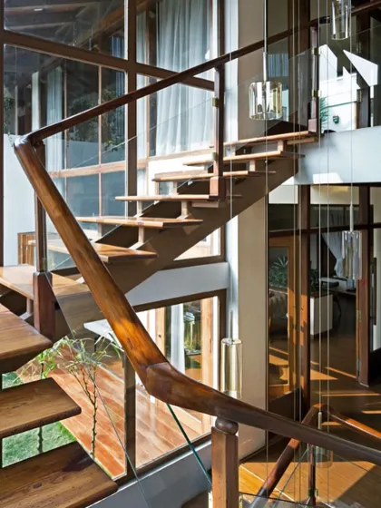 The staircase is a key feature, crafted from local wood with glass railings to maintain an open feel. It demonstrates how structural elements can be beautifully integrated with the home's natural and transparent aesthetic.