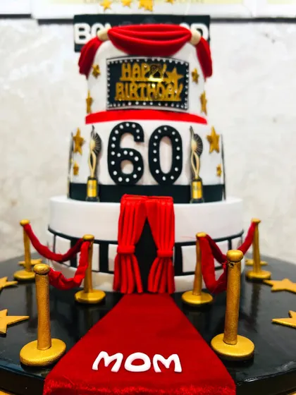 A close-up of the spectacular three-tier Bollywood-themed cake for a 60th birthday, showing the red carpet and velvet ropes.