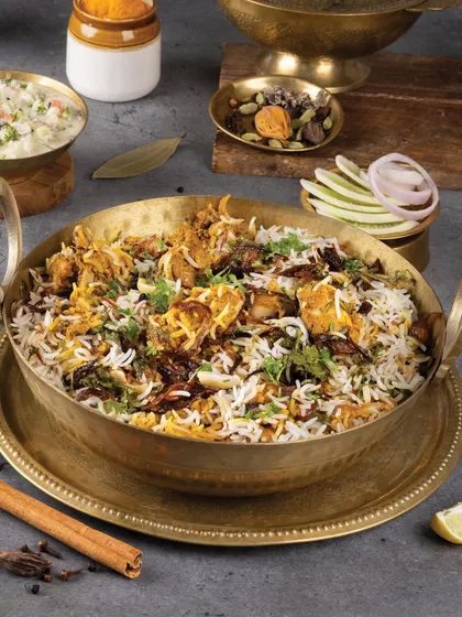 A magnificent brass pot of chicken biryani, garnished with fried onions and fresh herbs, looking like a royal feast.