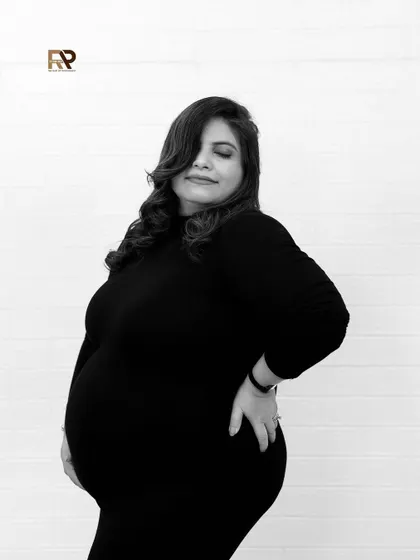 A timeless black and white portrait. The mom-to-be looks confident and beautiful in a simple black dress, her pose highlighting the stunning curves of pregnancy.