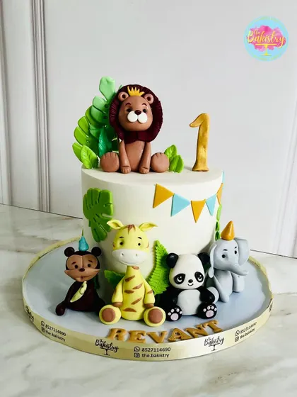 A premium jungle-themed first birthday cake for Revant. This design features a crowned lion king surrounded by his party-hat-wearing animal friends.