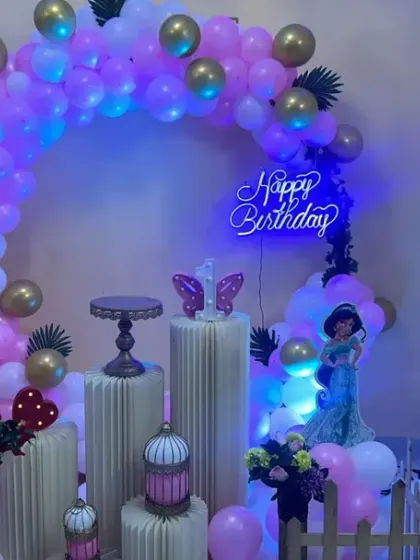 A princess-themed party with cool blue lighting. The pink and purple balloon arch is accented with a neon 'Happy Birthday' sign.