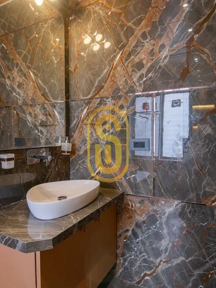 Another view of the dark marble bathroom, focusing on the vanity area. The uniquely shaped mirror and countertop sink add a touch of artistic flair to the functional space.