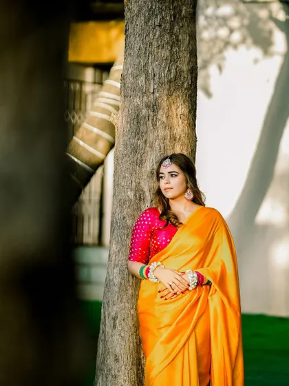A thoughtful portrait of the bride in her yellow Haldi saree, leaning against a tree. The natural setting and her relaxed pose create a serene and beautiful image.