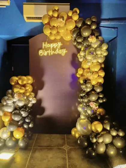 This stylish birthday decoration uses a black and gold balloon arch to create a bold statement. The "Happy Birthday" neon sign adds a modern touch, perfect for an evening celebration.