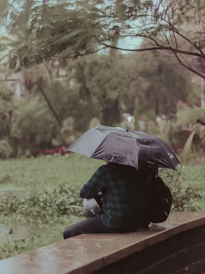 Someone finds a dry spot to sit and watch the rain, protected by their umbrella.