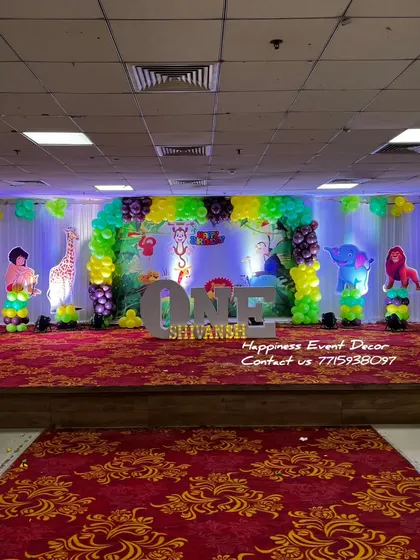 A wide-angle view of a jungle-themed birthday stage. The decor includes a large backdrop, balloon columns with animal cutouts, and 'ONE' in large letters, creating an immersive safari experience.