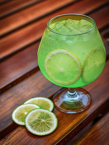 A close-up of a sparkling green lime mocktail on a wooden surface. The lighting highlights the condensation and bubbles, emphasizing how cool and refreshing the drink is.