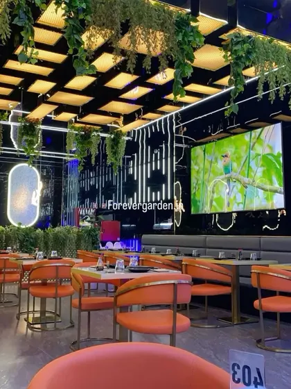 A modern restaurant with a black grid ceiling, decorated with hanging artificial ivy that adds a touch of green to the sleek, contemporary design.