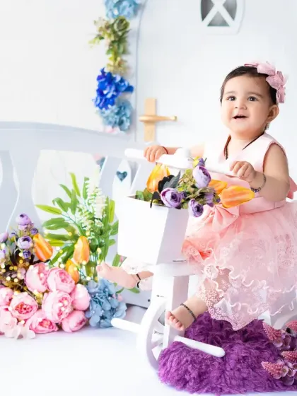 A beautiful portrait from a floral first birthday session. The combination of pink, blue, and purple flowers creates a vibrant and cheerful garden setting.