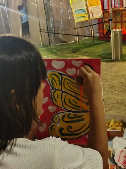A young artist concentrates on adding the finishing touches to her butterfly painting during an outdoor craft session.