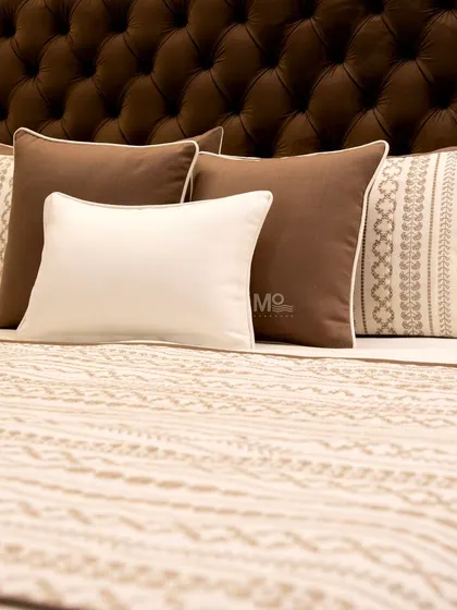 A beautifully styled bed featuring our patterned bedspread and a mix of solid brown and embroidered cushions against a tufted leather headboard. A perfect example of layering textures for a luxurious retreat.