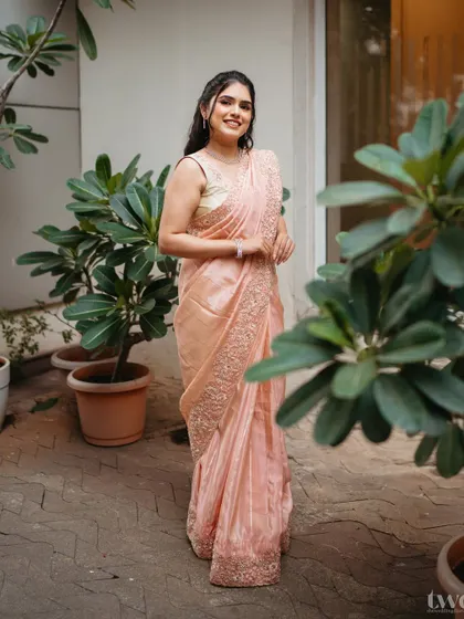 A full-length shot of the peach saree look. The makeup is kept dewy and fresh, complementing the soft color of the outfit.