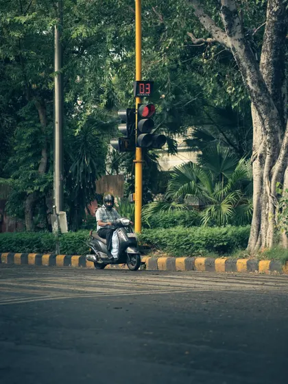 A lone scooter rider waiting at a red light on a gloomy day. The muted colors and solitary figure contribute to the overall moody and contemplative feel of the image.