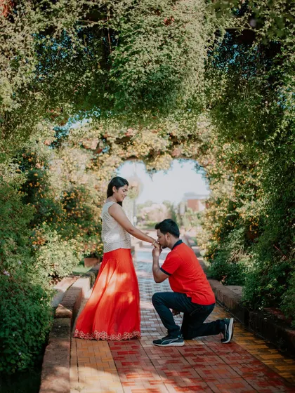 A classic romantic gesture as the groom-to-be kisses his partner's hand in a garden tunnel.