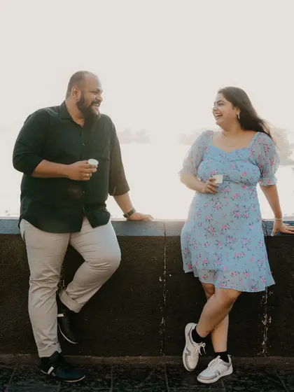 A relaxed moment of a couple leaning against a wall overlooking the Mumbai sea link, laughing and enjoying a cup of chai. This shows how we can capture casual, everyday romance.