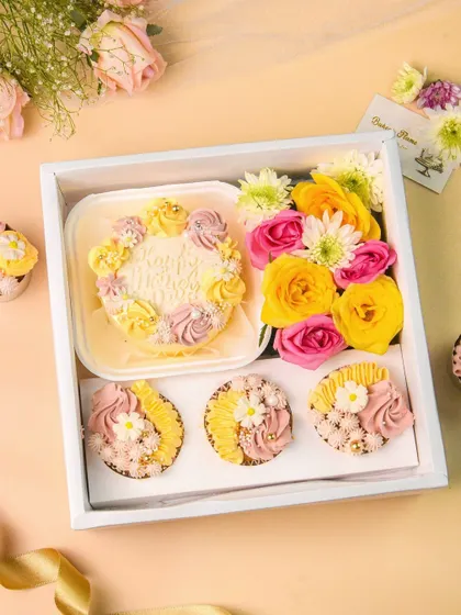 A beautiful bakery hamper featuring a mini-cake and matching cupcakes, arranged with fresh flowers. This flatlay is perfect for showcasing seasonal or celebratory gift boxes.