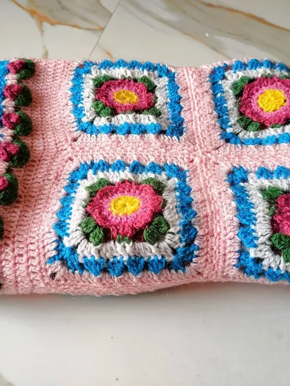 A folded view of the Lydia blanket, highlighting the texture of the stitches and the puffy rosebud border.