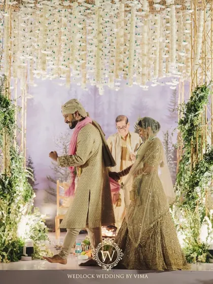 A candid moment from a beautiful minimalist wedding. The couple is framed by the modern mandap, which features a canopy of white florals against a backdrop of a misty forest.