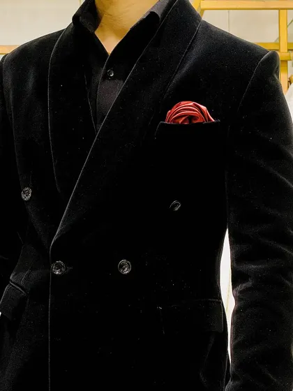 A close-up of a timeless black velvet double-breasted tuxedo. The deep black fabric and the pop of a red silk pocket square create a look of pure, old-school class.
