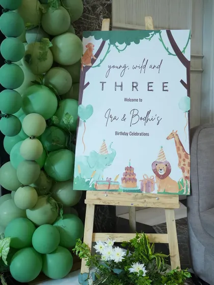 A personalized welcome sign on an easel, framed by a cascade of green balloons, greeted guests for Ira and Bodhi's "Young, Wild and Three" birthday celebration. It's a small touch that makes a big first impression.