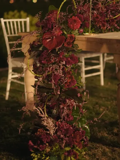 A detail of the table decor, featuring a lush runner of red flowers cascading down the side of a rustic wooden table.