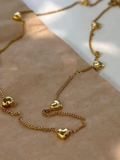 A lovely gold-toned necklace featuring small, puffy heart charms spaced along a delicate chain. This romantic piece is perfect for gifting or as a treat for yourself.