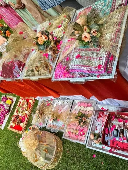 A wide shot of a complete trousseau set laid out for a wedding event. You can see the variety in packaging, from large fabric-wrapped trays to smaller transparent boxes, all decorated with fresh flowers.