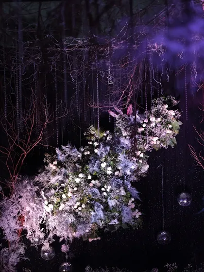 A moody, artistic shot of the enchanted forest decor. The purple smoke adds to the mystical atmosphere, highlighting the textures of the floral arrangement and hanging branches.