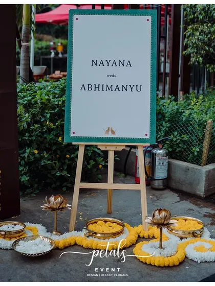 A simple and elegant welcome board, surrounded by marigold and jasmine petals and traditional lotus-shaped lamps.
